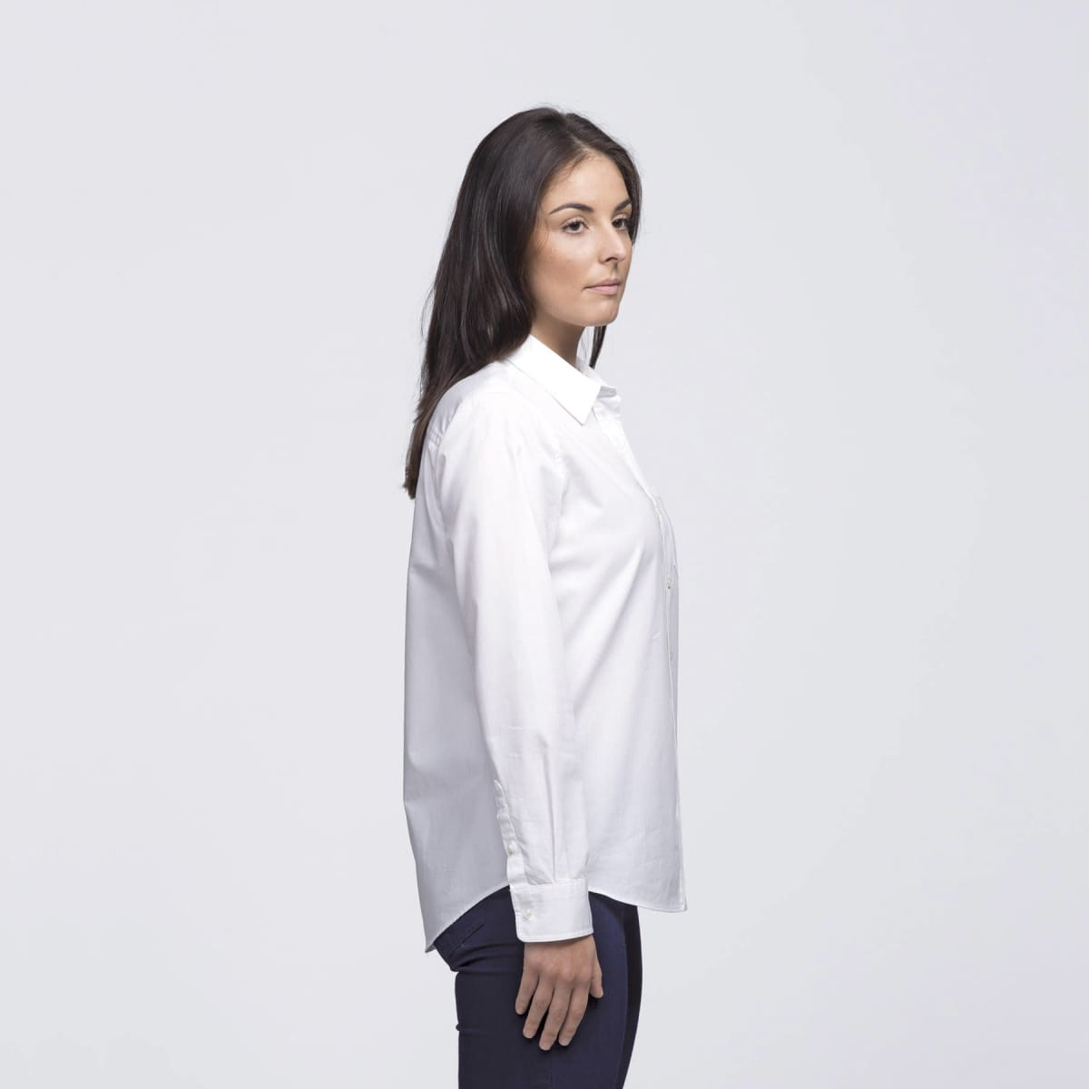A white button-up shirt on a woman, featuring a simple design and a logo on the shirt.