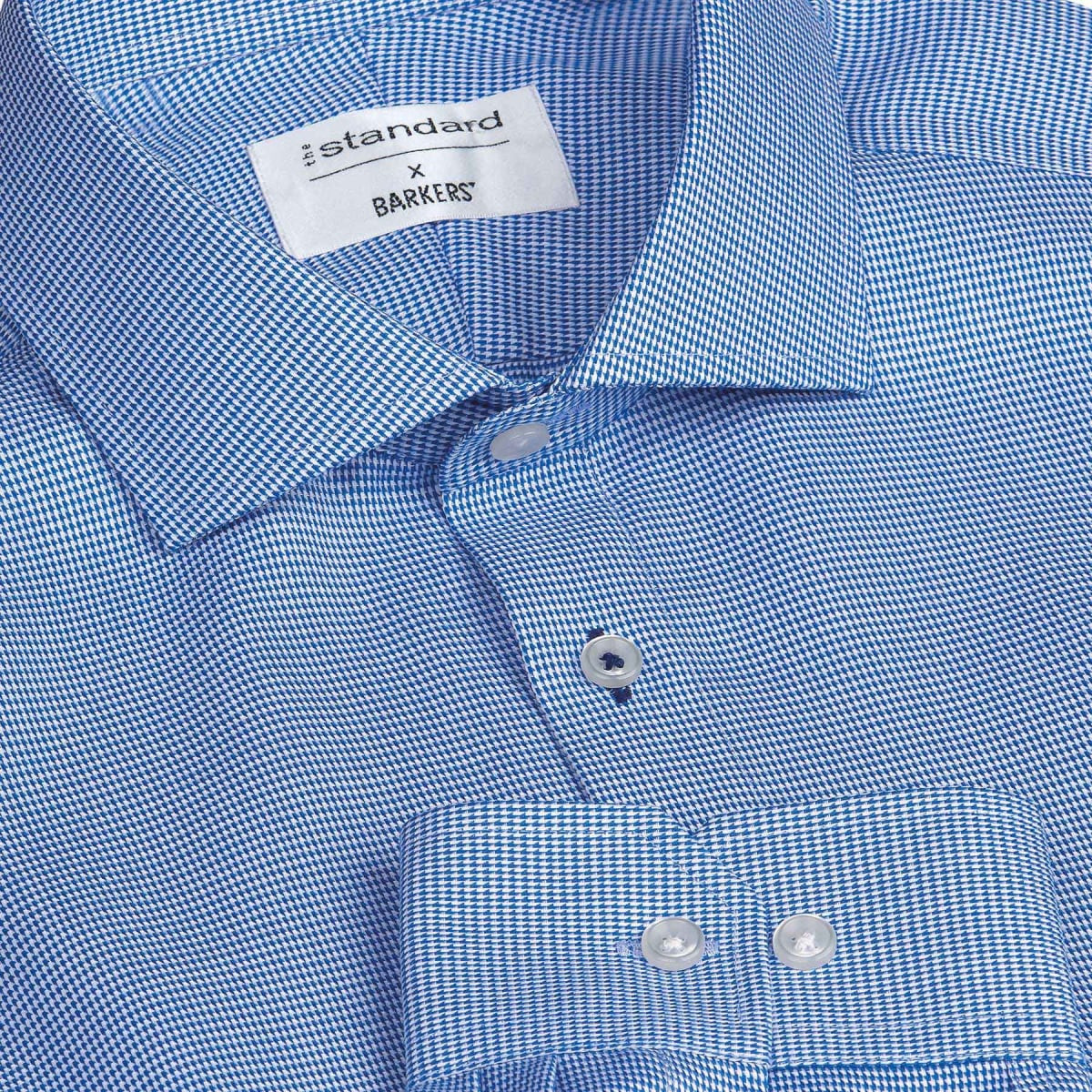 A blue check patterned button-up shirt with a collar and two buttons visible at the front, featuring a logo label.
