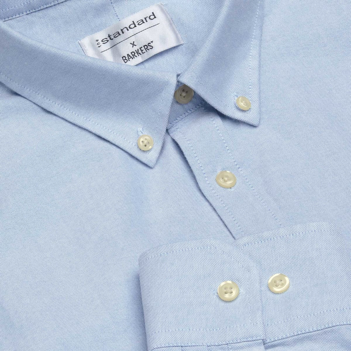 A light blue button-up shirt with a collar, featuring a branding label and light-coloured buttons.