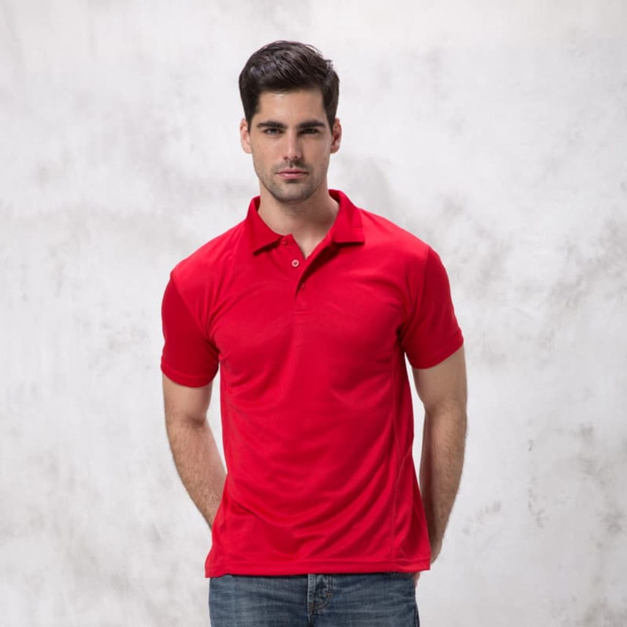 A red polo shirt worn by a man, standing with hands at his sides against a textured background. The shirt features a collar and branding.