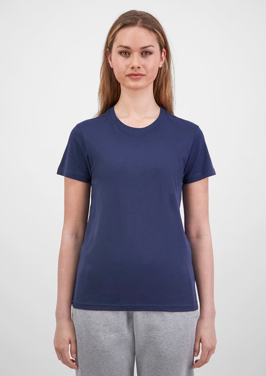 A woman stands wearing a navy short sleeve tee, paired with grey sweatpants, featuring a logo on the tee.