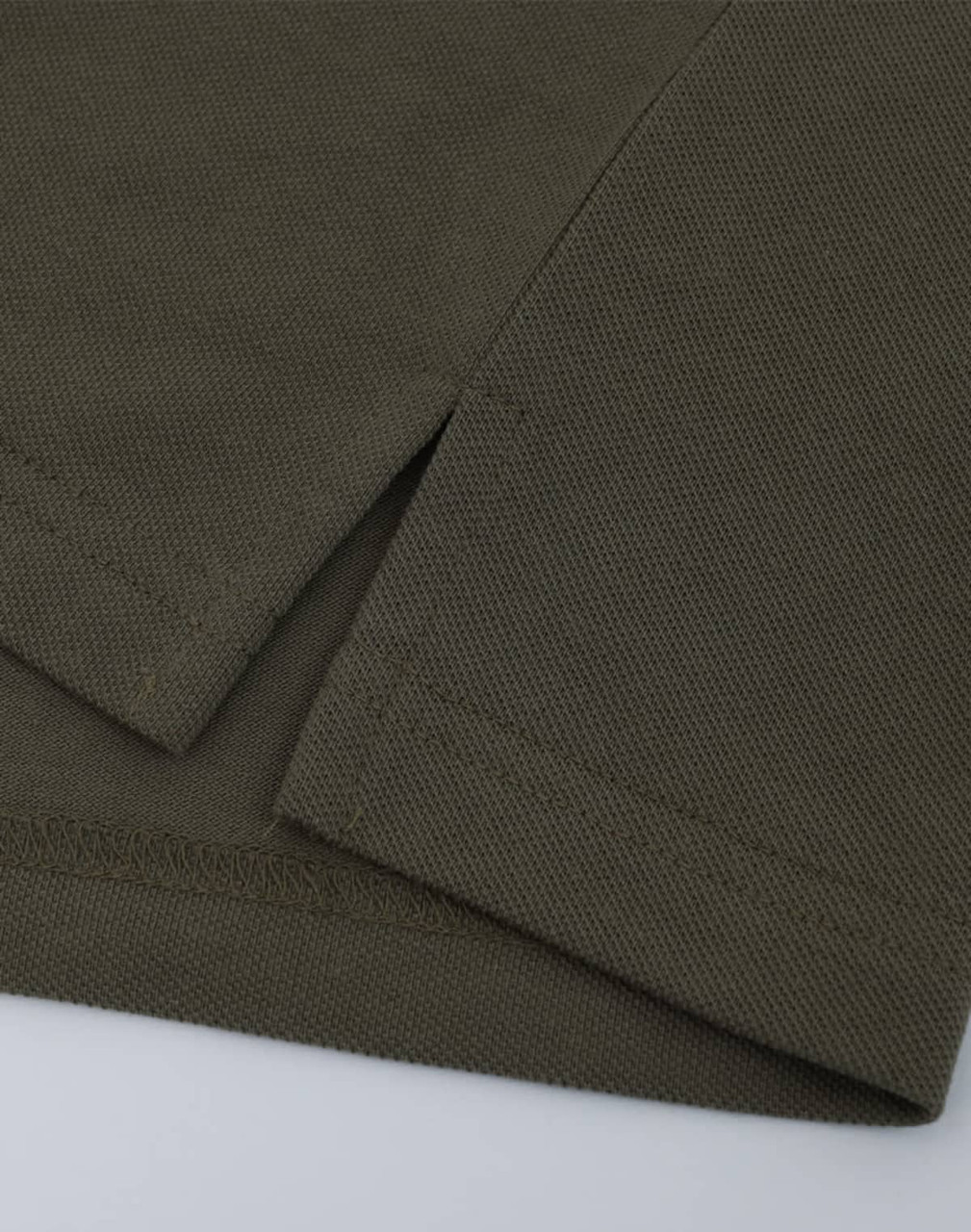 A close-up of a short-sleeved polo in an olive green cotton/poly pique fabric with a stitched hem.