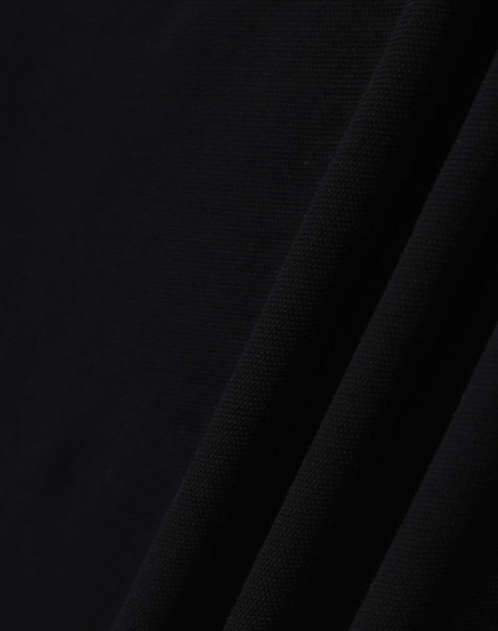 A close-up of black ultrafine cotton pique fabric, textured with a smooth finish. It features subtle folds.