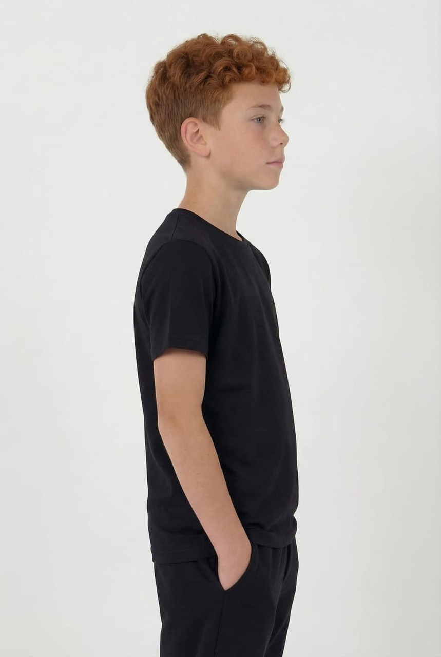 A youth in a black tee stands sideways, featuring short sleeves and a simple design. The outfit includes matching black shorts.
