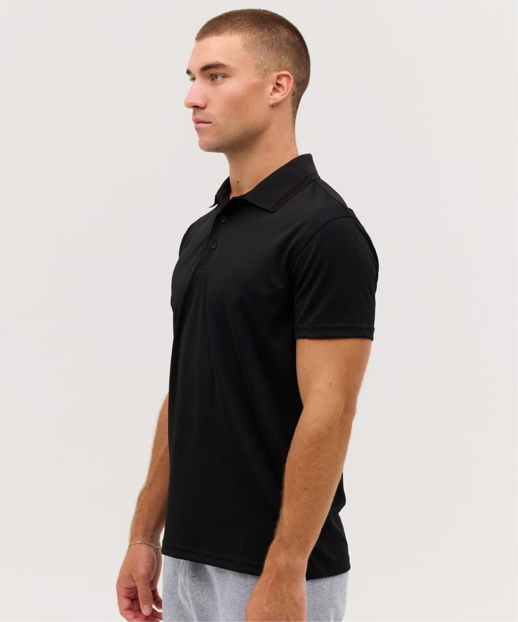 A black polo shirt displayed on a male model, featuring a collar and short sleeves. The shirt has a logo.