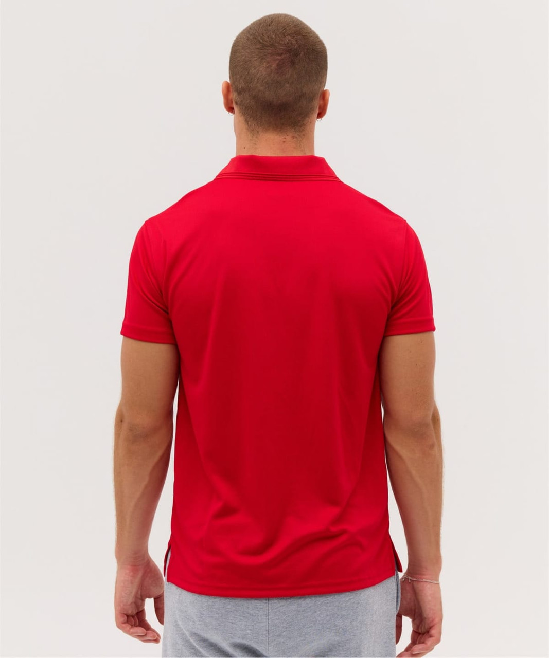 A red polo shirt viewed from the back, featuring a fitted design and a collar. There is a logo present on the shirt.
