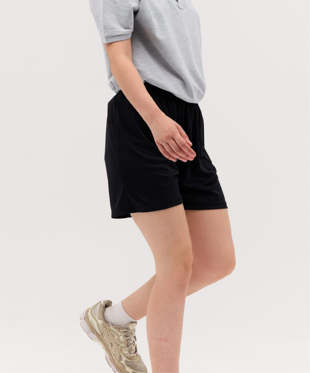 Black sports shorts are featured, paired with a grey top and light-coloured sneakers. The shorts have an elastic waistband.
