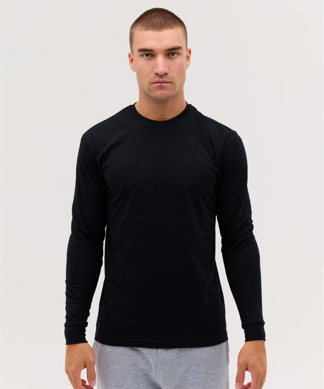 A long sleeve black tee features a fitted design and includes a logo. Model is wearing grey pants.