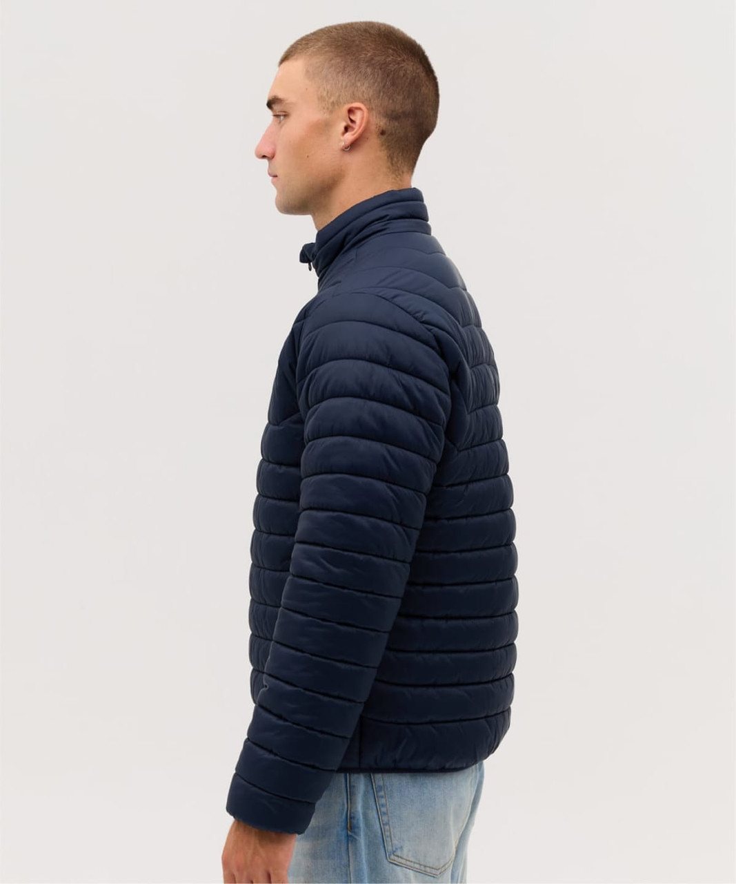 A man wearing a navy blue puffer jacket, facing sideways, showcasing its quilted design and high collar.