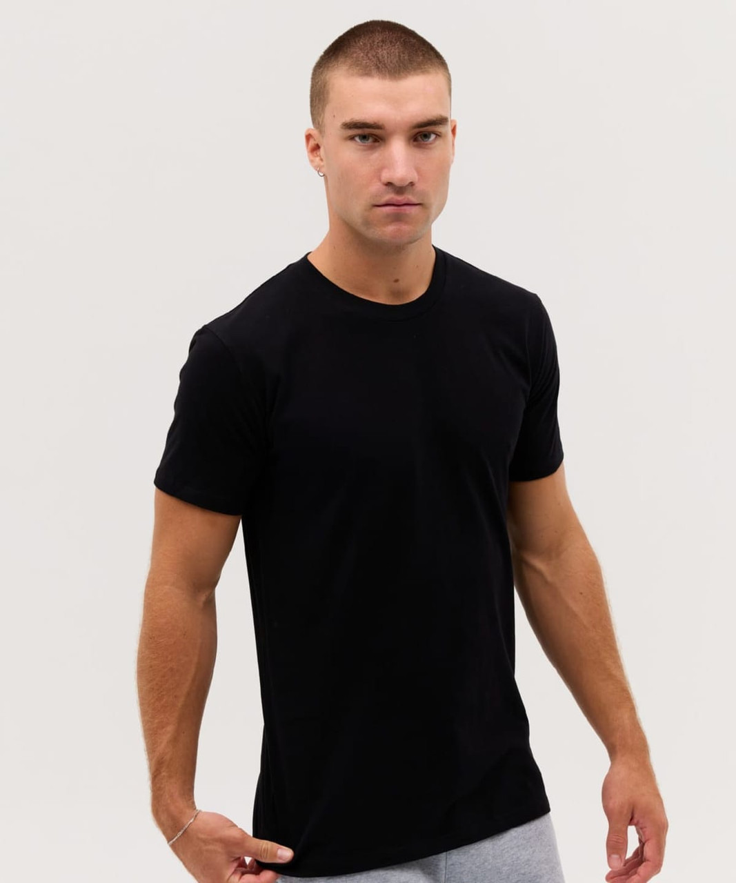 A plain black t-shirt on a model, featuring a slim fit and short sleeves. The model has short hair and a neutral expression.