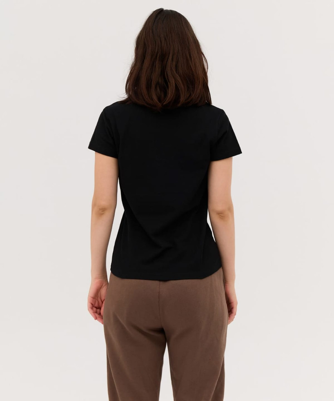A black women's polo shirt featured from the back, paired with brown pants. It has a simple design and fits snugly.