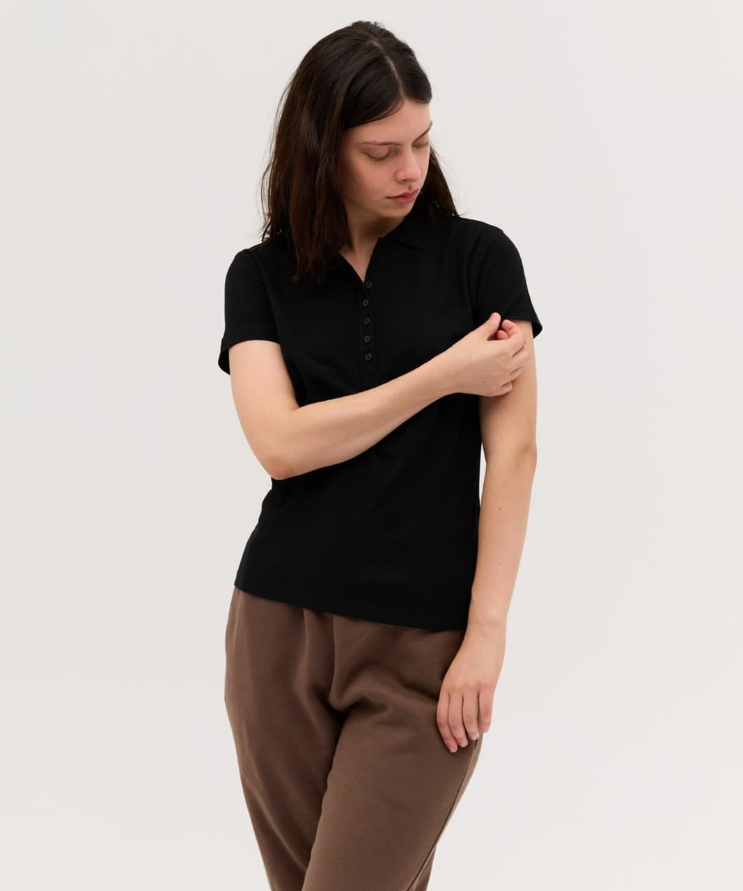 A black women's polo shirt with a button-up front, showcased by a model wearing casual pants.