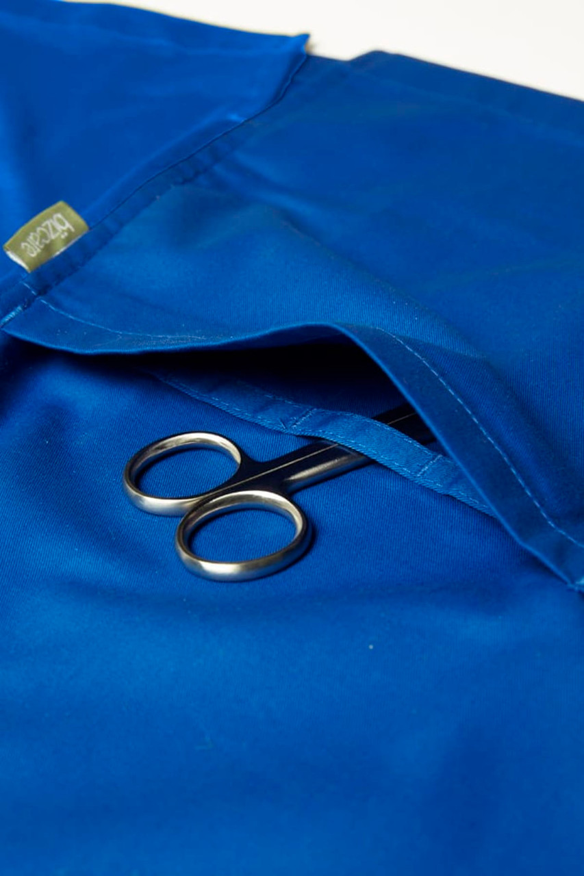 A blue women's scrub top with a pocket containing a pair of scissors and featuring a logo.