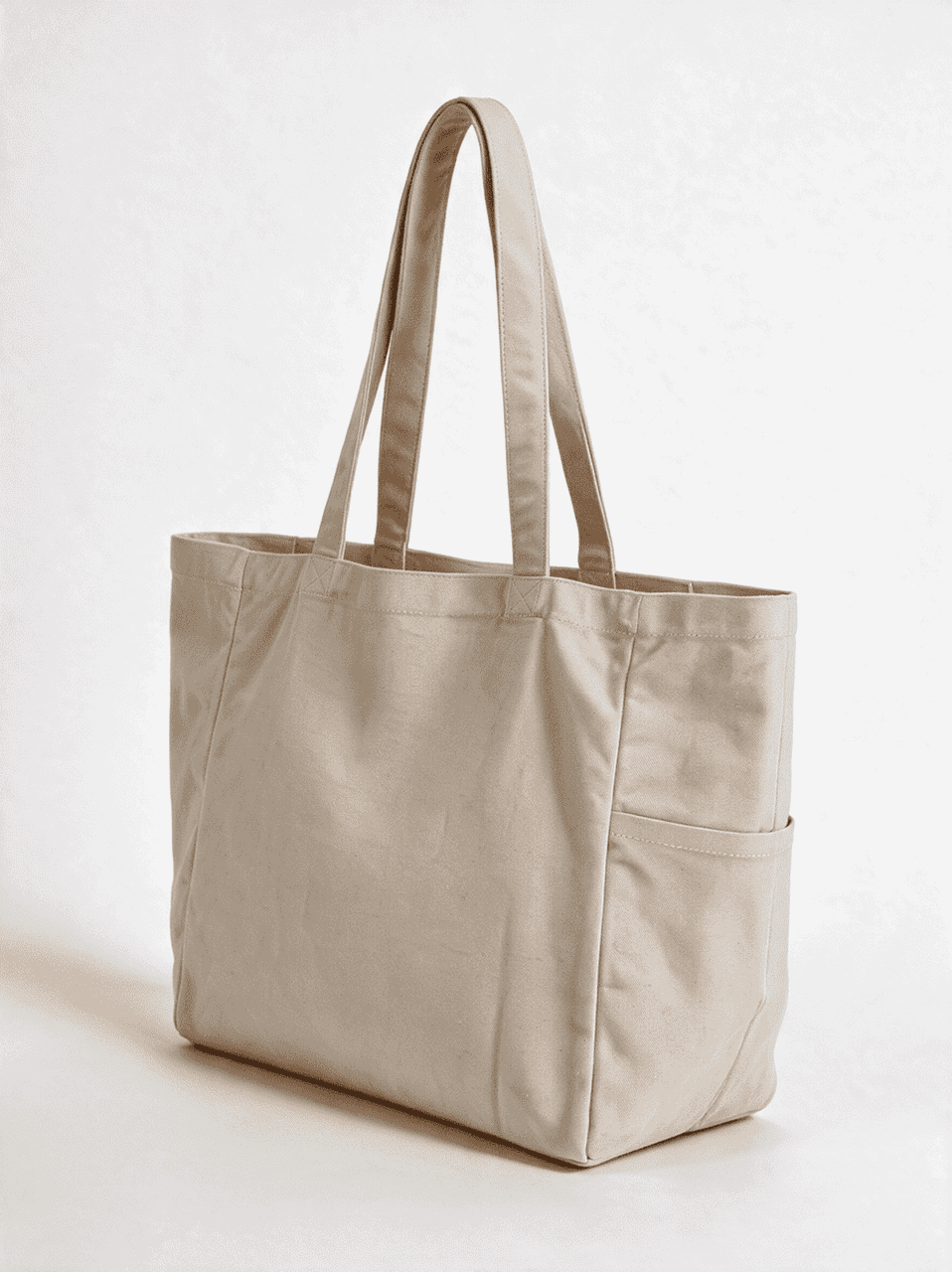 A light beige canvas tote bag with two handles and a side pocket, featuring a logo.