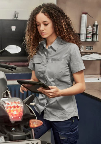 Lightweight grey short sleeve shirt for women, featuring a front button closure and a logo, displayed in a workshop setting.