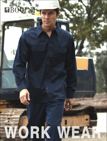 A model wearing navy unisex cotton drill work pants with a matching shirt and a hard hat. The background features construction equipment.