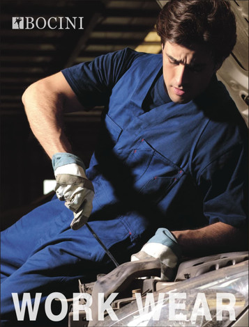 A man wearing a navy cotton drill overall, using tools while working on a vehicle. The overall has a logo.