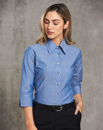 A fitted ladies' chambray shirt in blue with a button-up front and 3/4 sleeves, featuring a simple collar and branding.