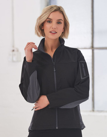A black softshell jacket with grey accents, featuring a zip front and a side pocket, worn by a model indoors.