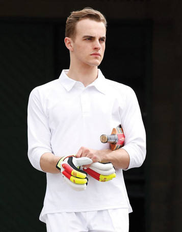 A white men's 3/4 sleeve cricket polo with a logo, worn by a model holding a cricket bat and gloves.