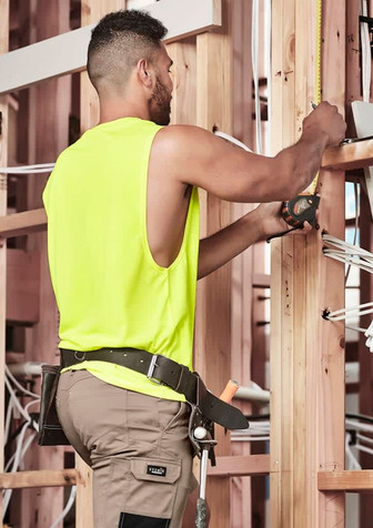 A sleeveless high-visibility yellow tee worn by a man working on a construction site, measuring with a tool.