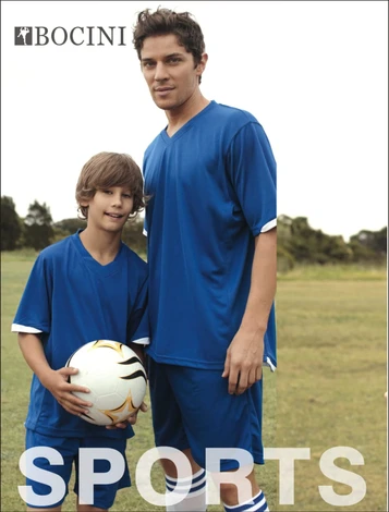 A pair of individuals in blue sports shirts are standing on a grassy field, holding a soccer ball.