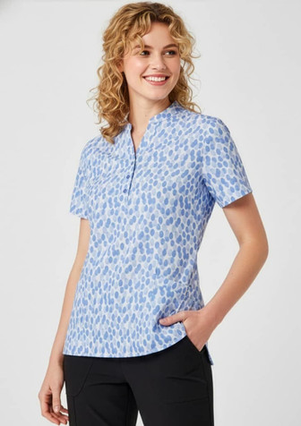 A blue tunic with a stardust print, featuring short sleeves and a collar, displayed on a smiling model.