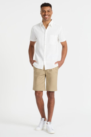 A model wearing beige chino shorts and a white short-sleeved shirt, paired with white sneakers. Logo visible.