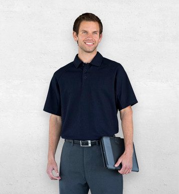 A man wearing a navy Dri Gear Summit Coolmax polo, paired with dark trousers and holding a tablet, stands against a neutral background.