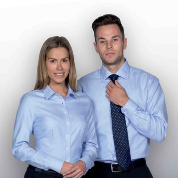 A man and woman are wearing light blue button-up shirts, with the man also wearing a dark polka dot tie.