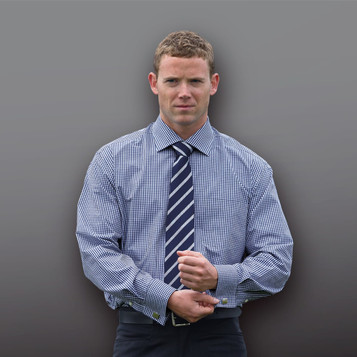 A man in a blue and white checked button-up shirt with a navy tie, posed against a grey background.