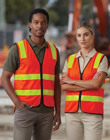 A high-visibility safety vest in bright orange with reflective strips, worn by two individuals on a construction site.