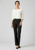 A woman stands in sleek black slacks paired with a light-coloured top and heels, showcasing a stylish look.