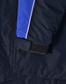 A close-up of a navy jacket featuring blue and white detailing, with a Velcro cuff closure. It has a logo on it.