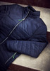 A navy blue quilted jacket with a high collar and a green zip pull, laid flat on a textured surface.