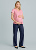 A pregnant woman wears a pink top and navy maternity pants, standing with one hand on her belly. The background is neutral.