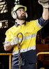 A man wearing a high-visibility yellow and navy long sleeve shirt with reflective tape, safety glasses, and hearing protection.