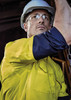 A men’s closed front long sleeve shirt in yellow and navy, featuring a logo, worn with safety goggles and a hard hat.