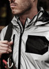 A reflective silver waterproof jacket with a black pocket, featuring a high collar and zip closure, worn by a model.