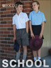 A boy in a white school shirt and grey shorts stands next to a girl in a blue shirt and black skirt, both smiling.