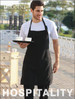 A black cotton drill full bib apron without pockets, worn by a man holding a tray with cups.