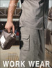 A person holds a jerry can while wearing grey cotton drill cargo work pants featuring multiple pockets and branding.