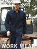 A model wearing navy unisex cotton drill work pants with a matching shirt and a hard hat. The background features construction equipment.