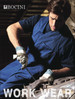 A man wearing a navy cotton drill overall, using tools while working on a vehicle. The overall has a logo.