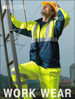 A man in a hi-vis yellow and navy jacket and pants, wearing a hard hat, stands on a ladder outdoors.