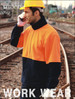 A man wearing a high-visibility orange and navy polar fleece jacket, equipped with a yellow safety helmet and gloves, standing near railway tracks.