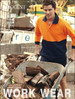 A man in an orange and navy long-sleeve polo shirt pushes a wheelbarrow filled with timber at a worksite.