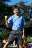 A boy in a light blue short sleeve school shirt and grey shorts stands proudly outdoors, smiling with a fist raised.