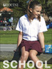 A girl wearing a white short sleeve school shirt and maroon skirt, sitting on a bench outdoors, with a logo visible.