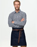 A man in a checkered shirt wears a denim half apron with a brown tie belt. The apron features pockets and a logo.
